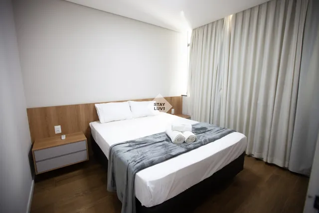 Sala de estar de apartamento moderno com sofá cinza e janelas amplas com vista para BH